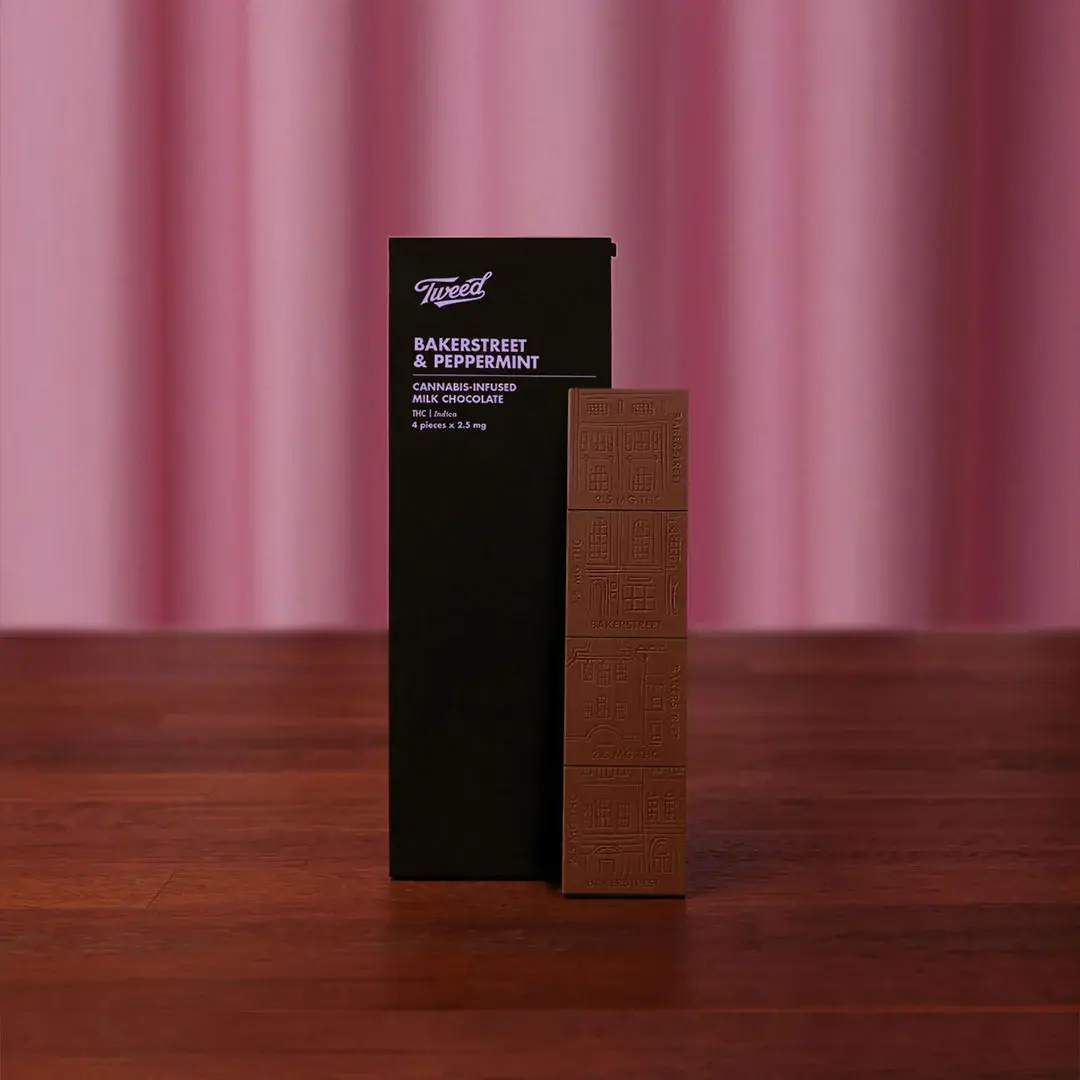 A box of Tweed cannabis-infused milk chocolate standing on a wooden table against a pink curtain.