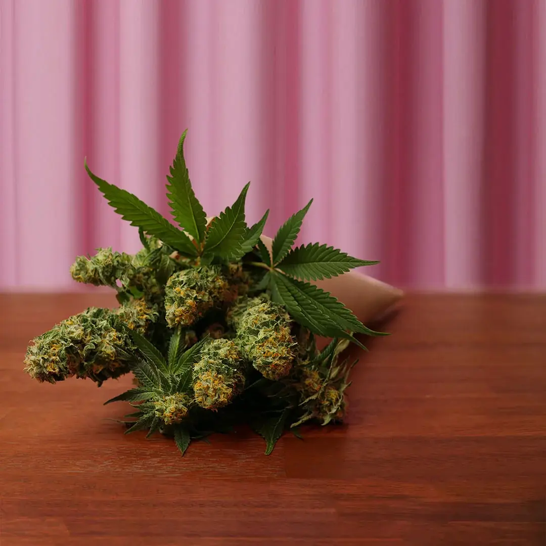 A bouquet of cannabis buds and leaves arranged like flowers on the same wooden table.