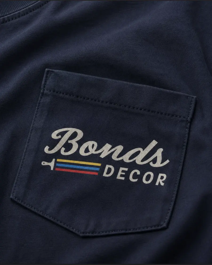 A navy pocket tee with the Bonds Decor script logo printed on the pocket in cream above a paintbrush trailing yellow, blue and red stripes.